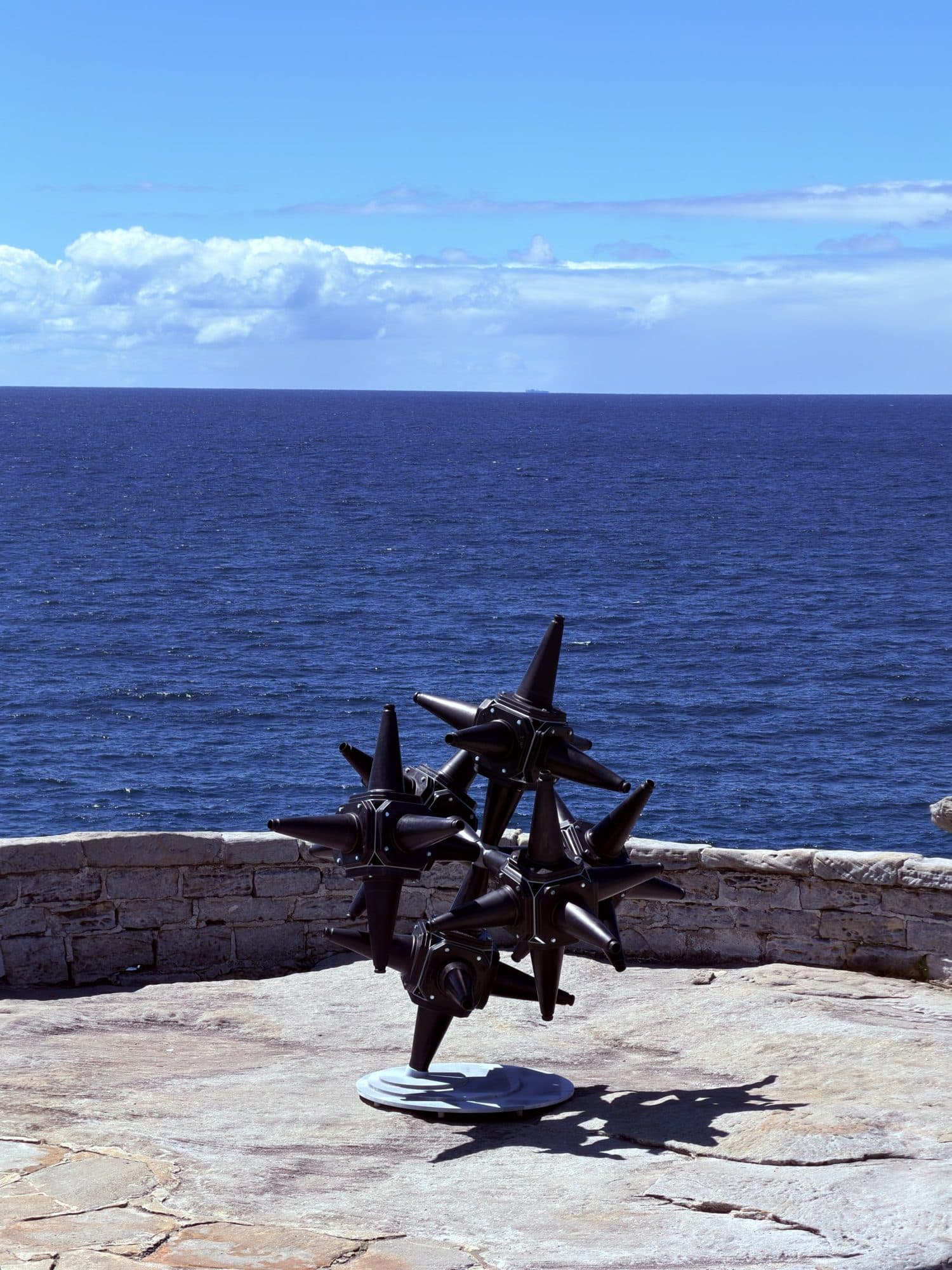 Lubo Mikle's H.T.S.: a cluster of black spiked star shapes on a thin stand, on a sandstone platform in front of a low wall and open ocean