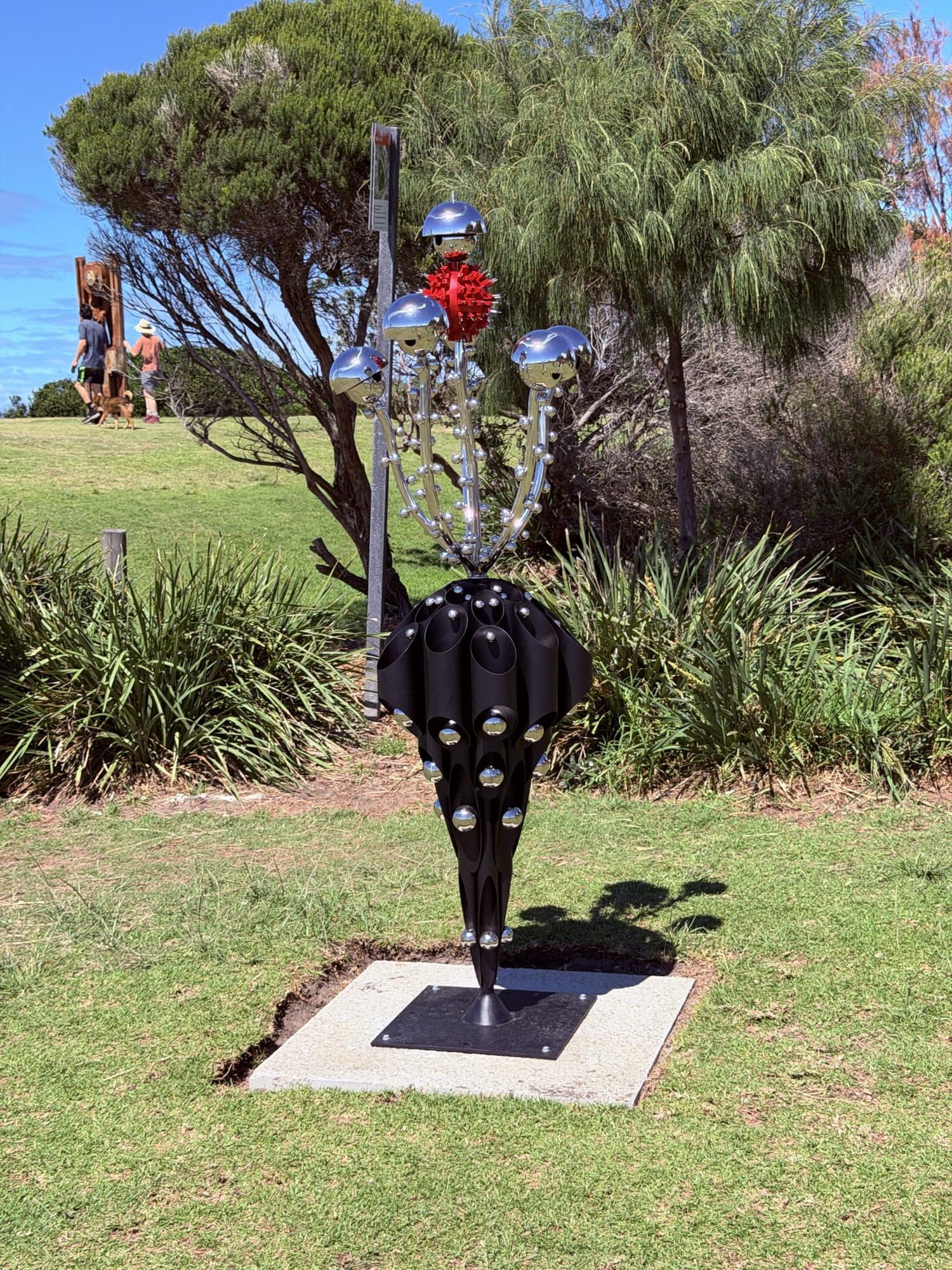 Shovin Bhattacharjee's Growth Within: a black studded pod with polished steel stems, mirror domes and a red flower, on the lawn at Marks Park