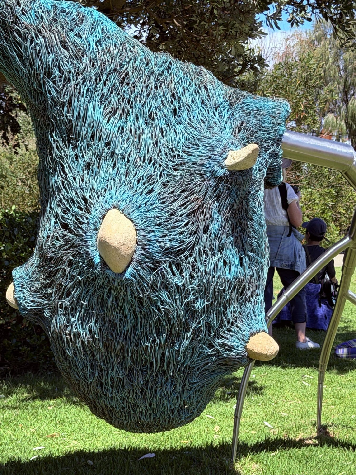 Close view of Bronwyn Berman's woven blue-green copper form, studded with pale river stones and hanging from silver steel branches