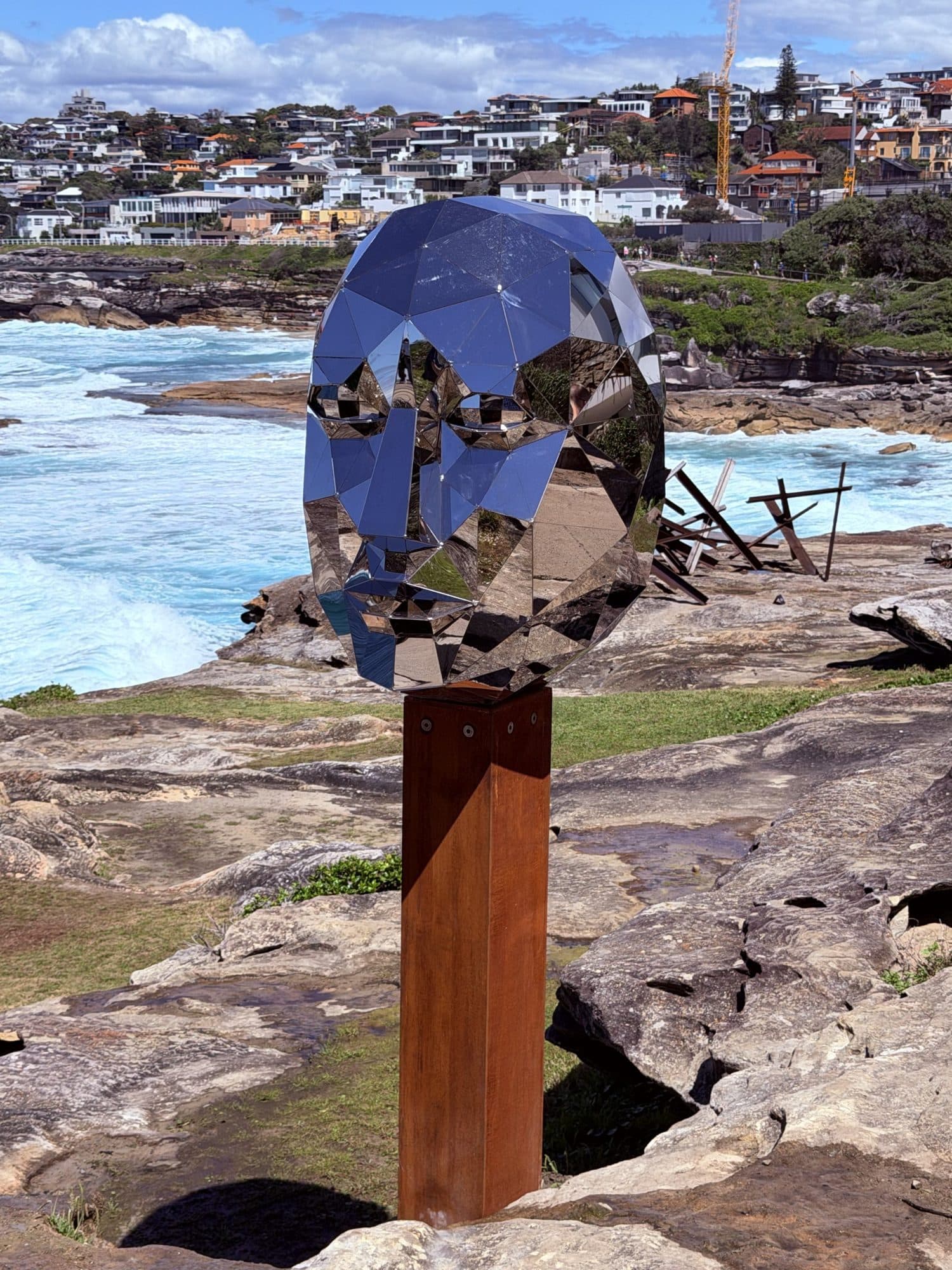 Paul Ewart's Both Sides Now: a faceted mirrored head on a rusted steel post, reflecting the surf and rocks below Bondi's southern headland